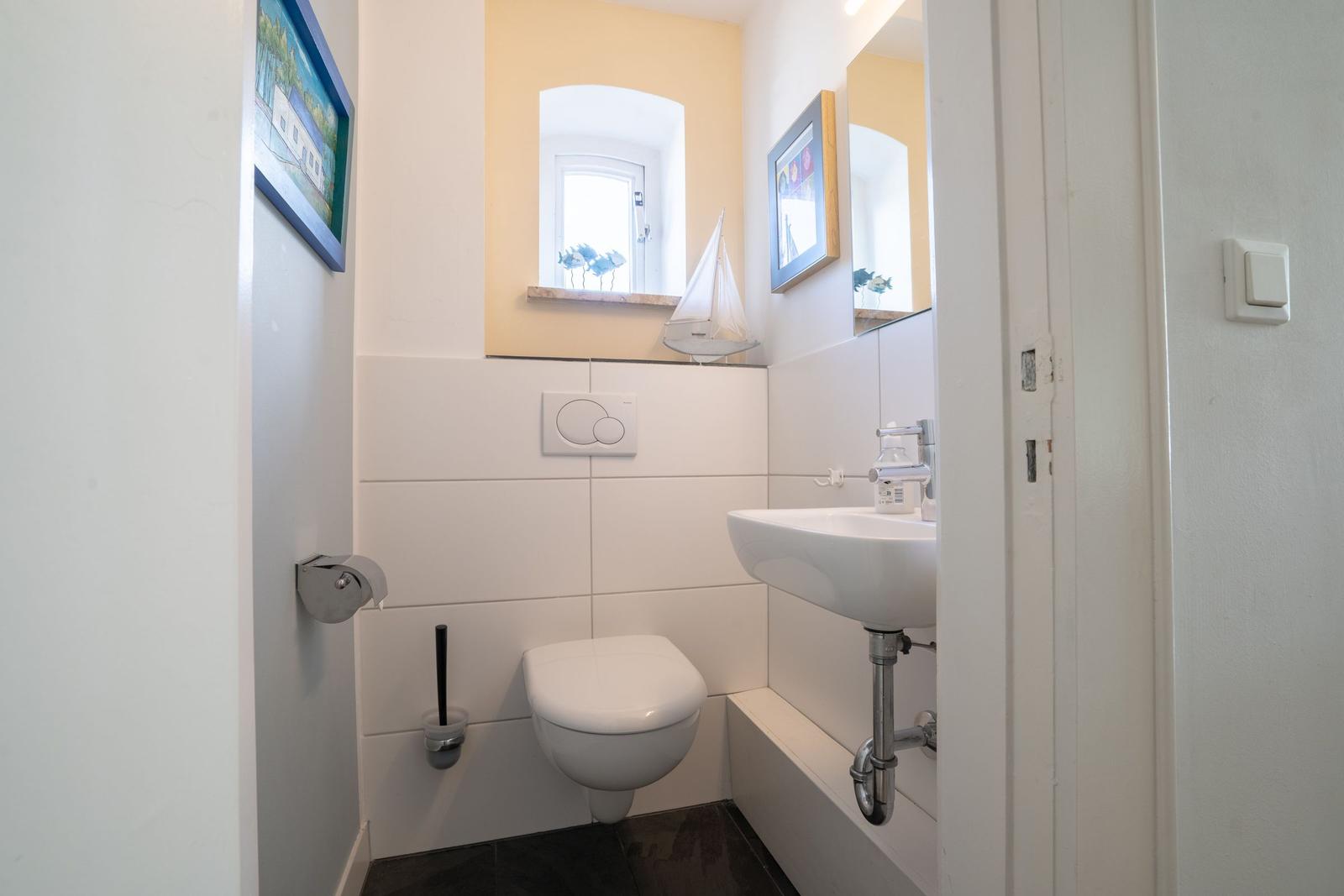 Bathroom with toilet, sink, and mirror. Wall decoration with pictures and window.