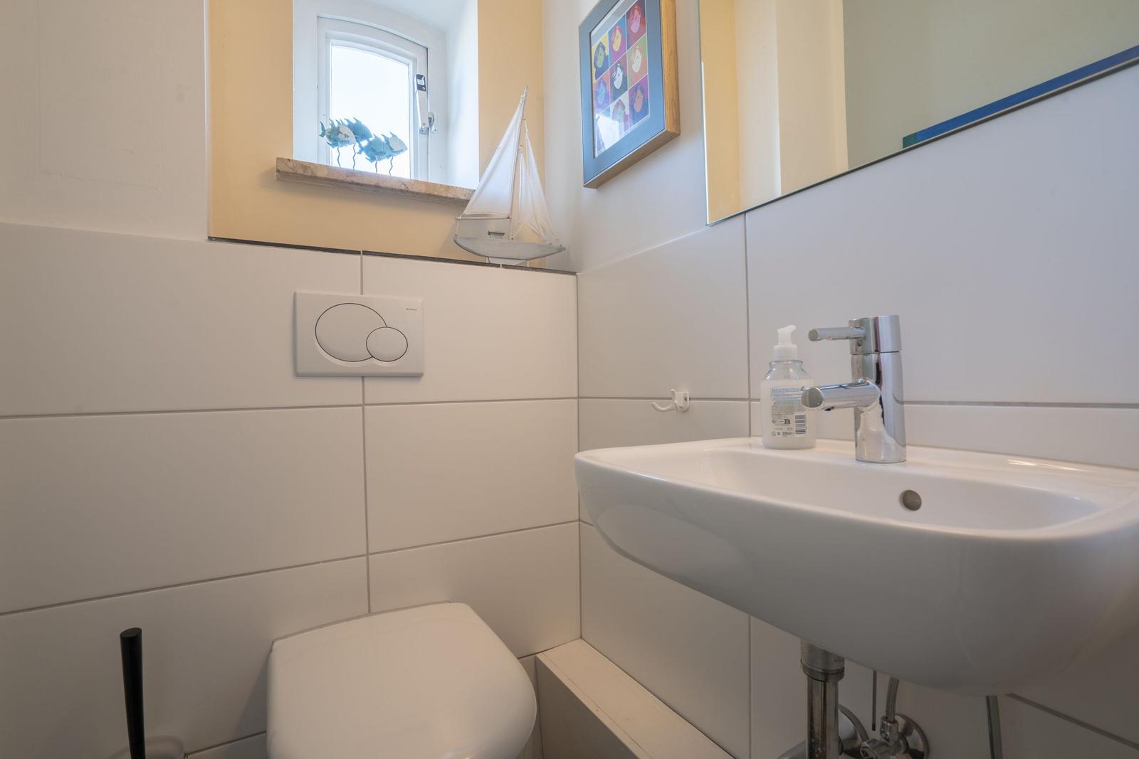 Bathroom with sink, toilet, and window with sailboat model.