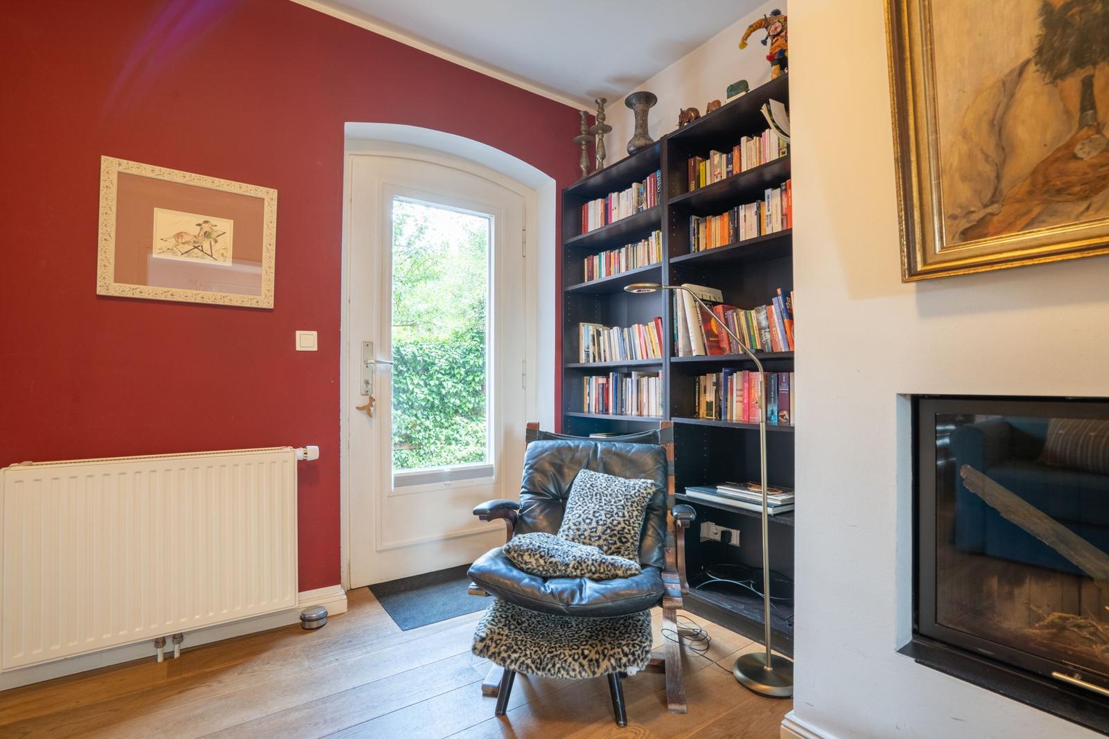 Room with red wall, bookcase, armchair, and fireplace.