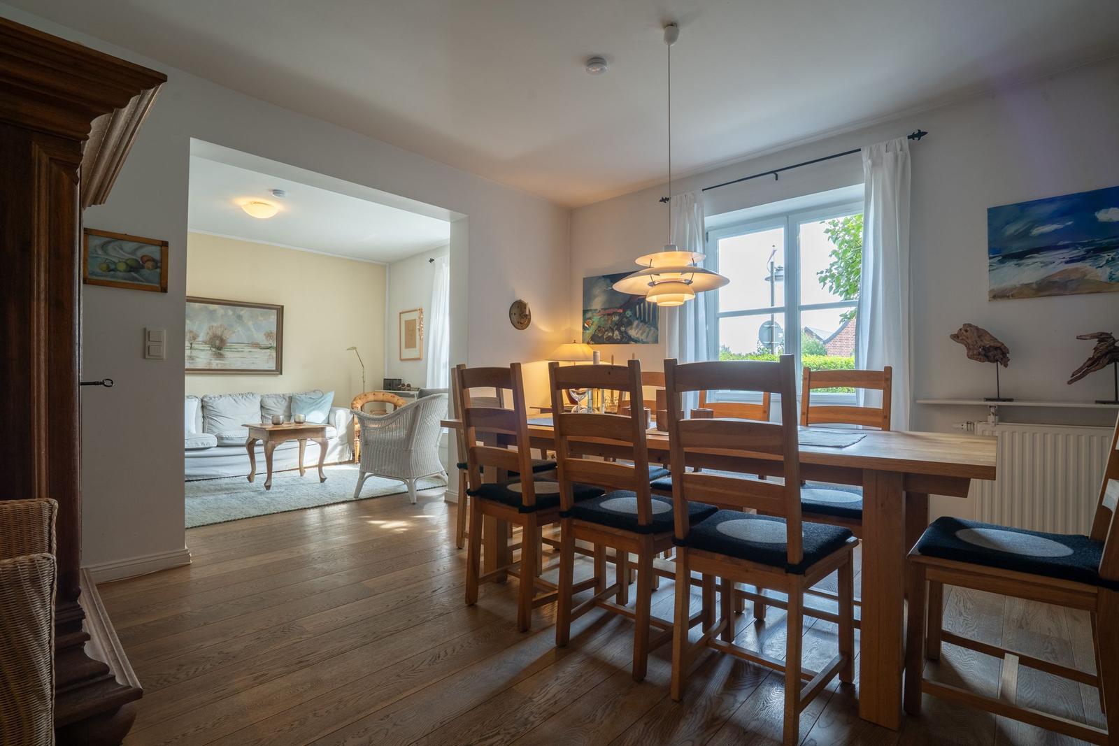 Dining room with wooden table and chairs, view into living room with sofa and rug.