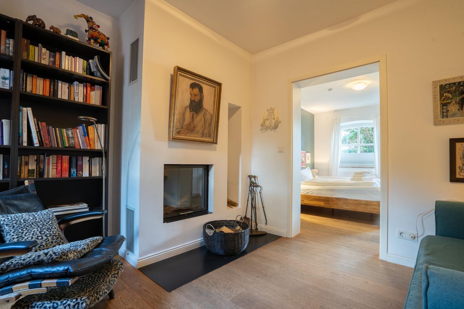 Living area with bookshelf, fireplace, and view into bedroom with bed.