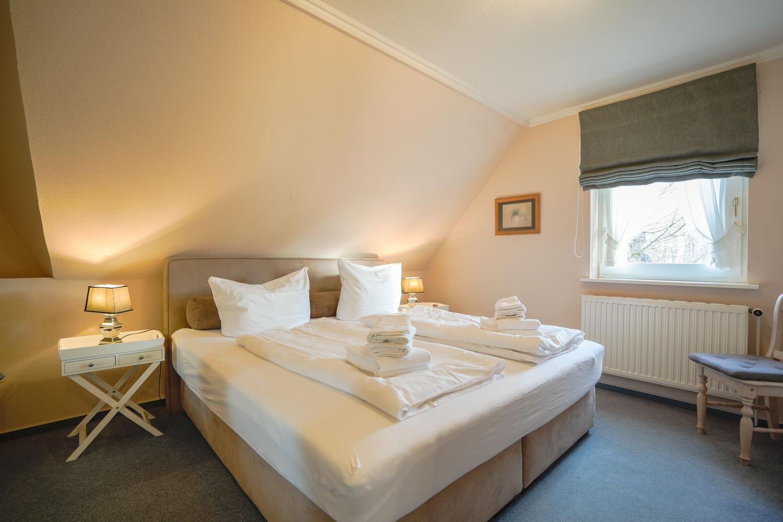 Schlafzimmer mit Doppelbett, Nachttisch und Fenster.