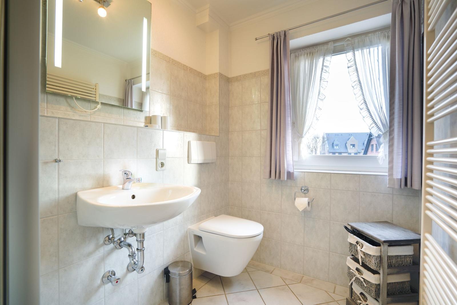 Badezimmer mit Waschbecken, Toilette und Fenster mit Vorhängen.