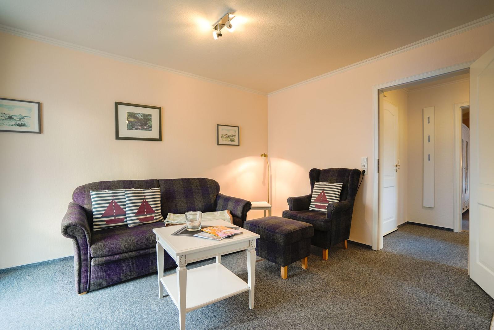Wohnzimmer mit Sofa, Sessel und Tisch. Wandbilder und Teppichboden.