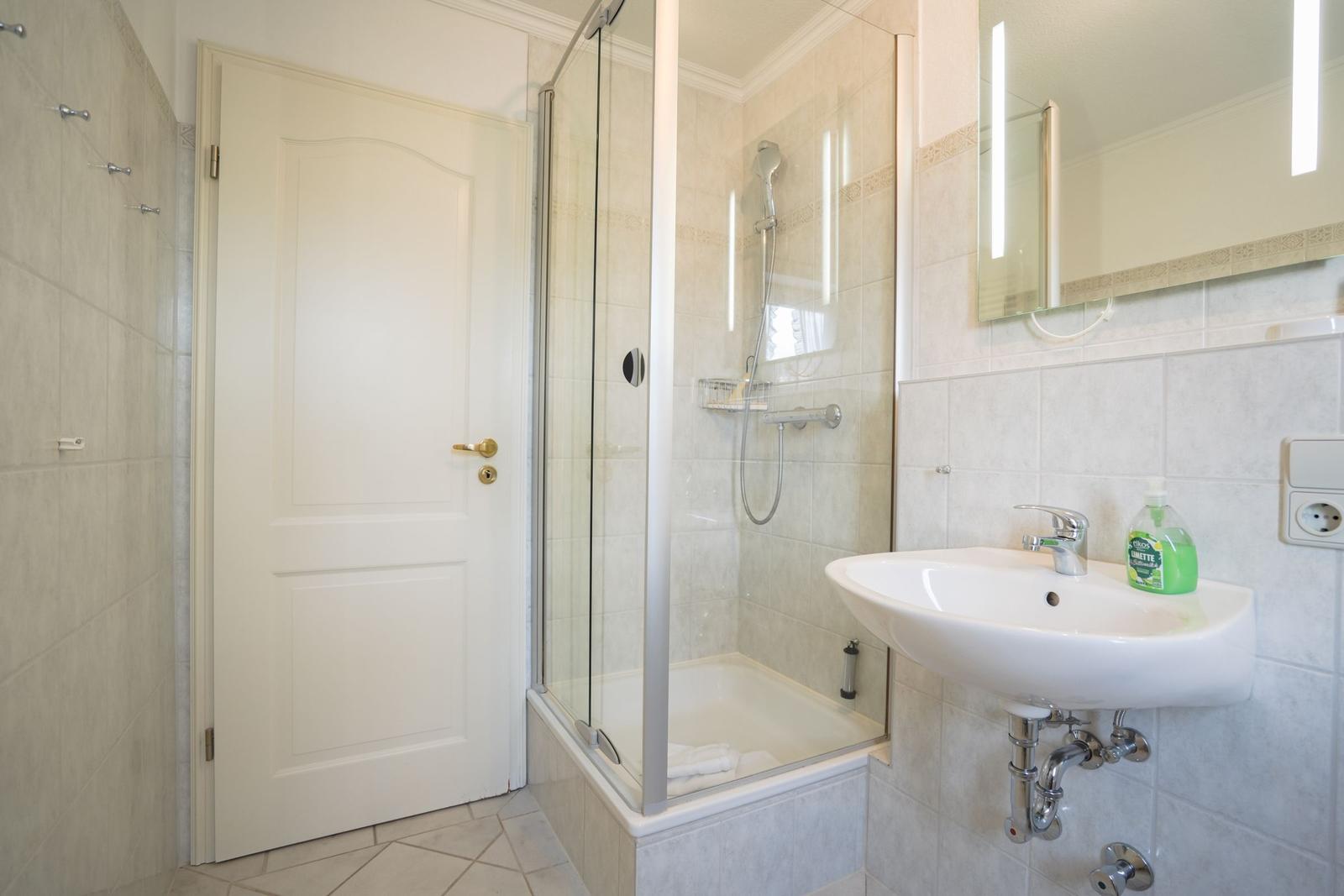 Badezimmer mit Dusche, Waschbecken und Spiegel.