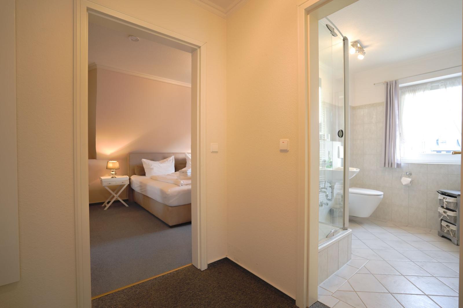 Schlafzimmer mit Bett und Nachttisch. Nebenraum mit Dusche und Toilette.