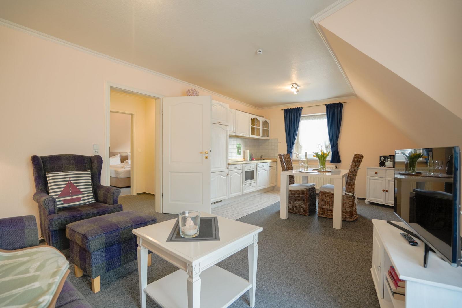 Wohnküche mit Esstisch, Sofa und TV. Tür führt zum Schlafzimmer.