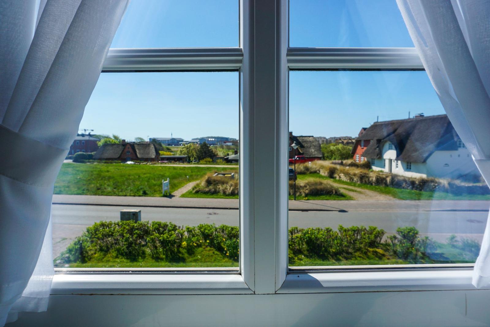 Durch das Fenster blickt man auf eine Straße mit Grünflächen und Häusern.