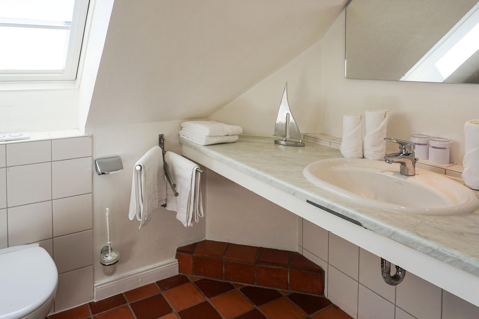 Badezimmer mit Waschbecken, Spiegel und Dachfenster. Terrakottafußboden und Handtücher.