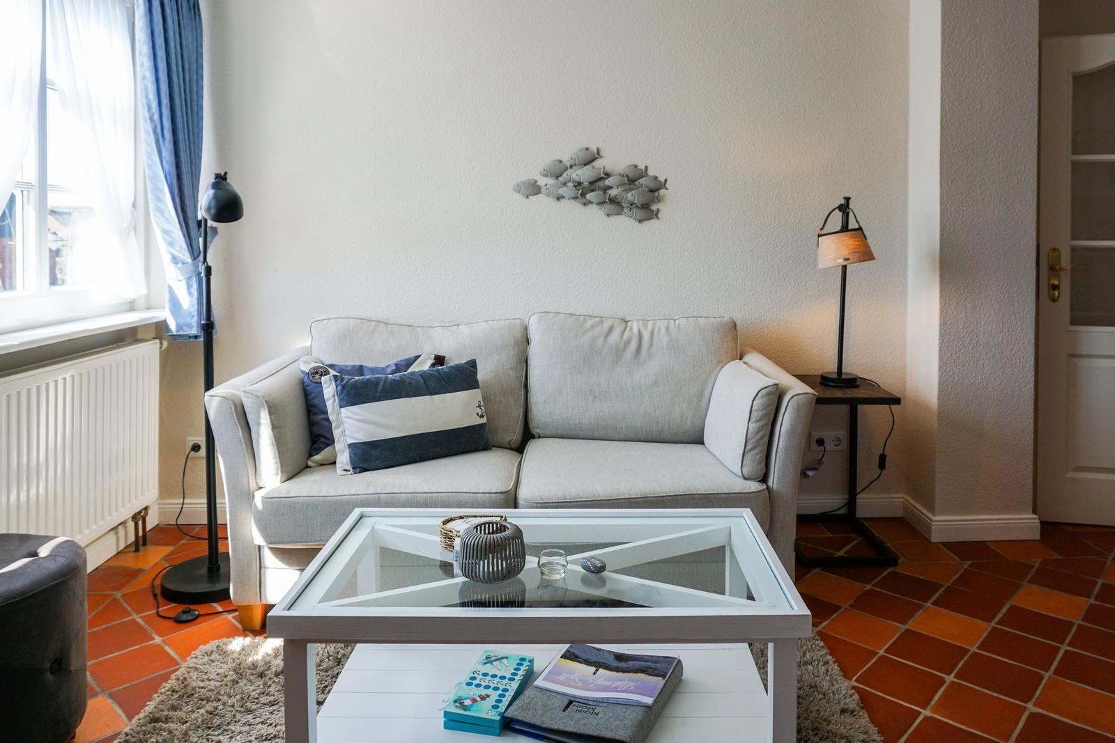 Ein Wohnzimmer mit einem Sofa, einem Glas-Tisch und einem Fenster.