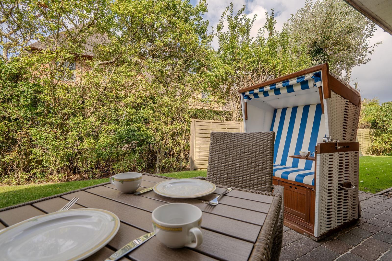 Terrace with table, chairs, and beach chair. Background: green area and fence.