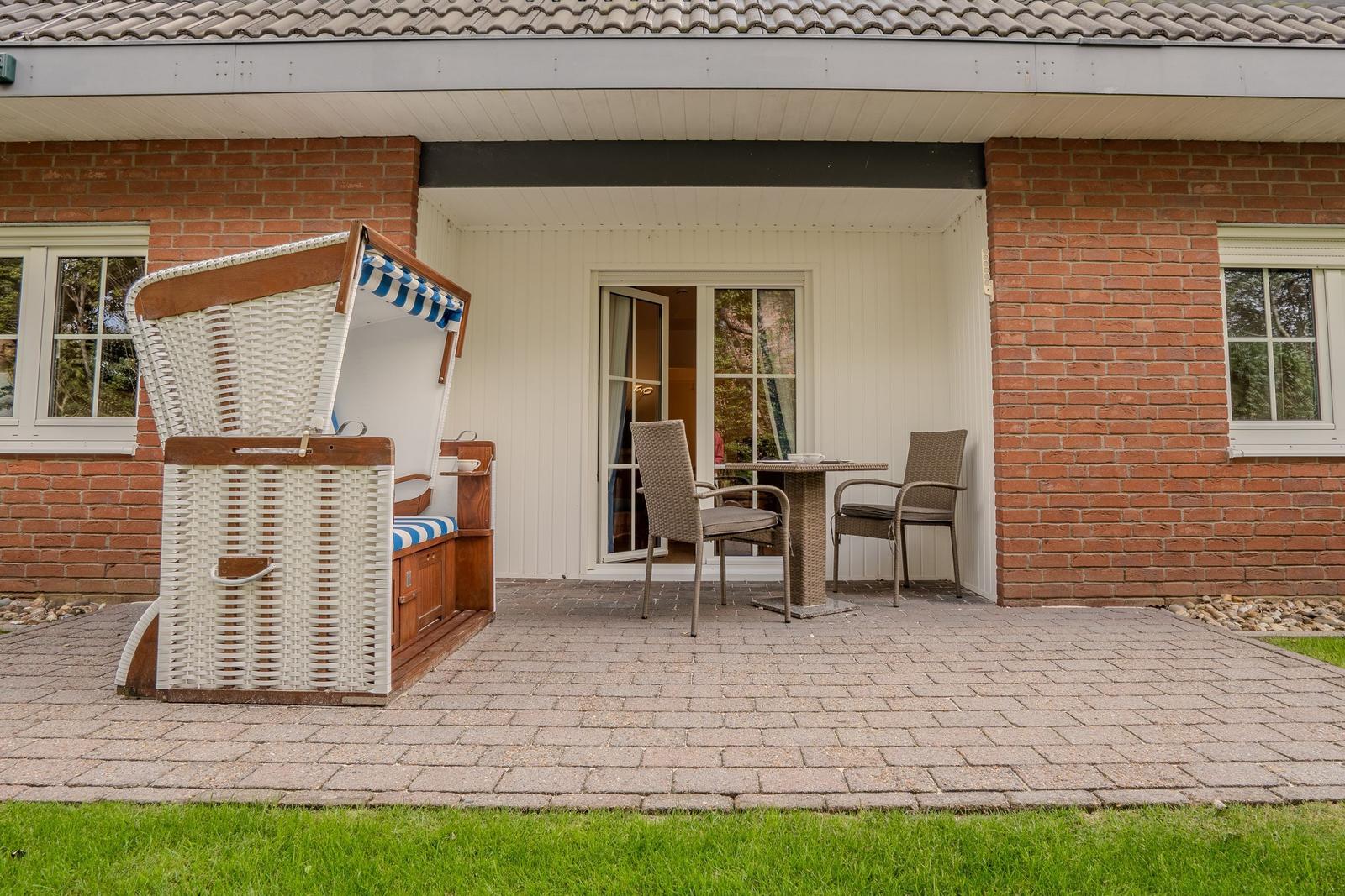 Terrace with beach chair and table with two chairs in front of house with brick wall.