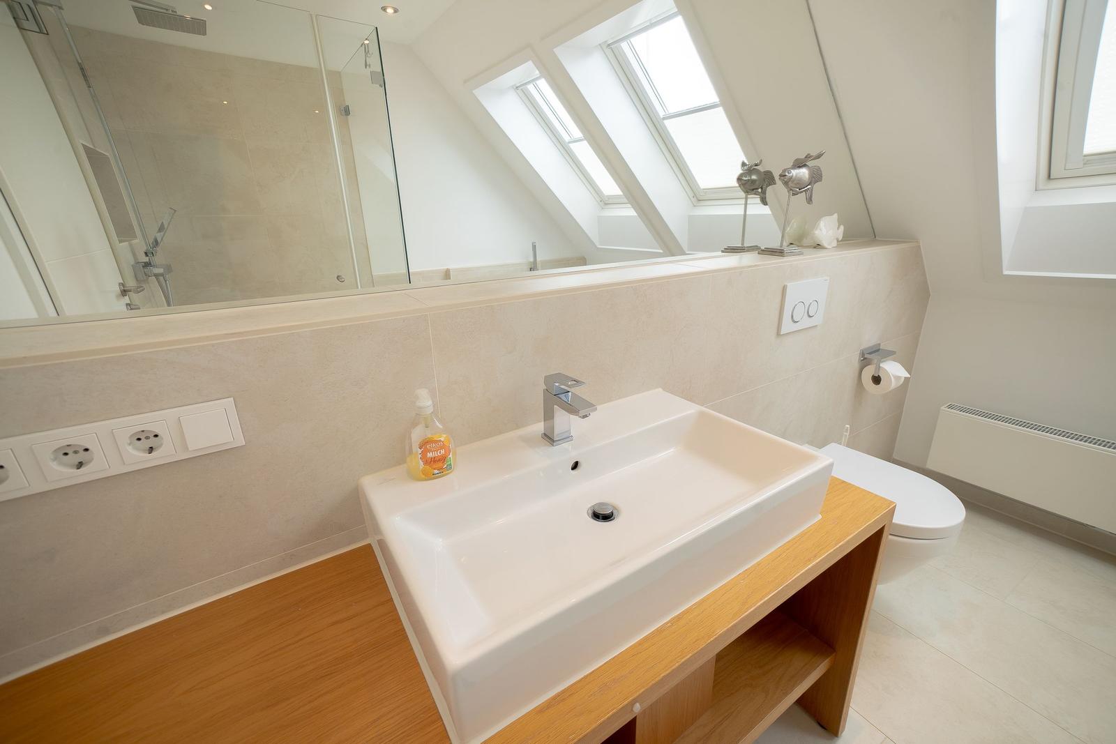 Badezimmer mit Waschbecken, Spiegel und Dusche unter Dachschrägen.