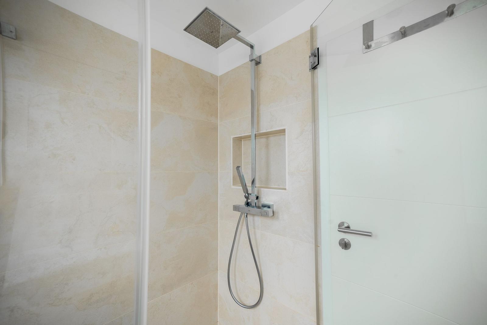 Dusche mit Duschbrause und Handbrause, beige Fliesen und Glaswand