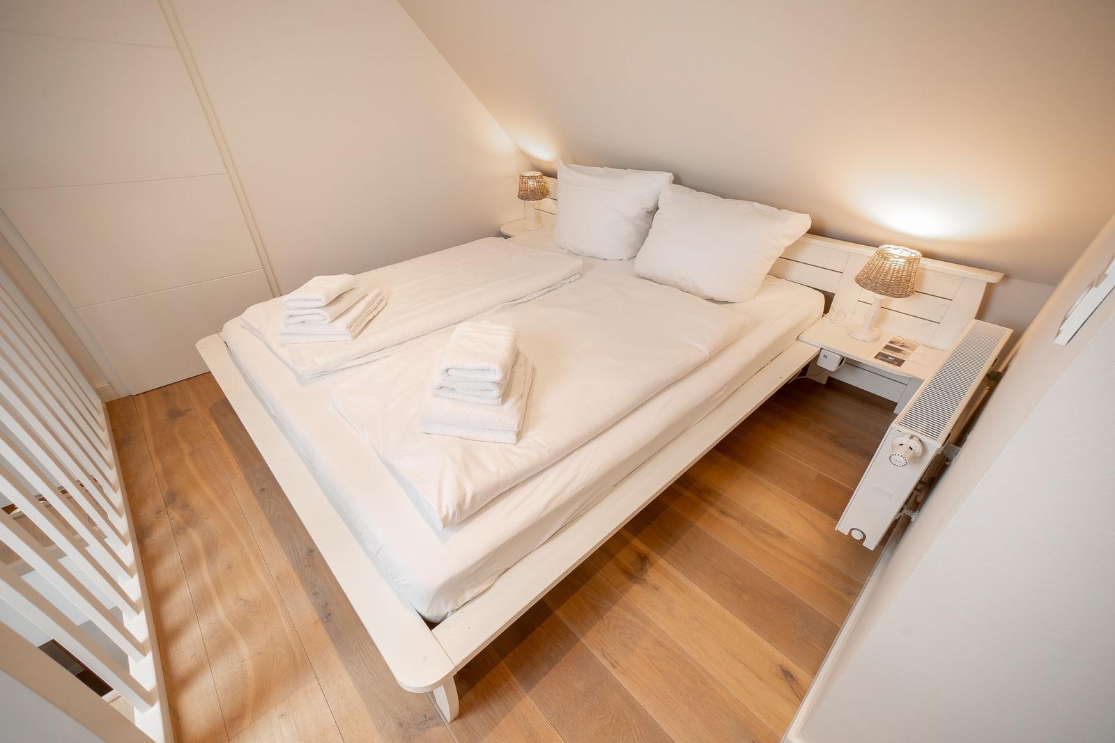 Schlafzimmer mit weißem Bett, Holzboden und Nachttisch mit Lampe.