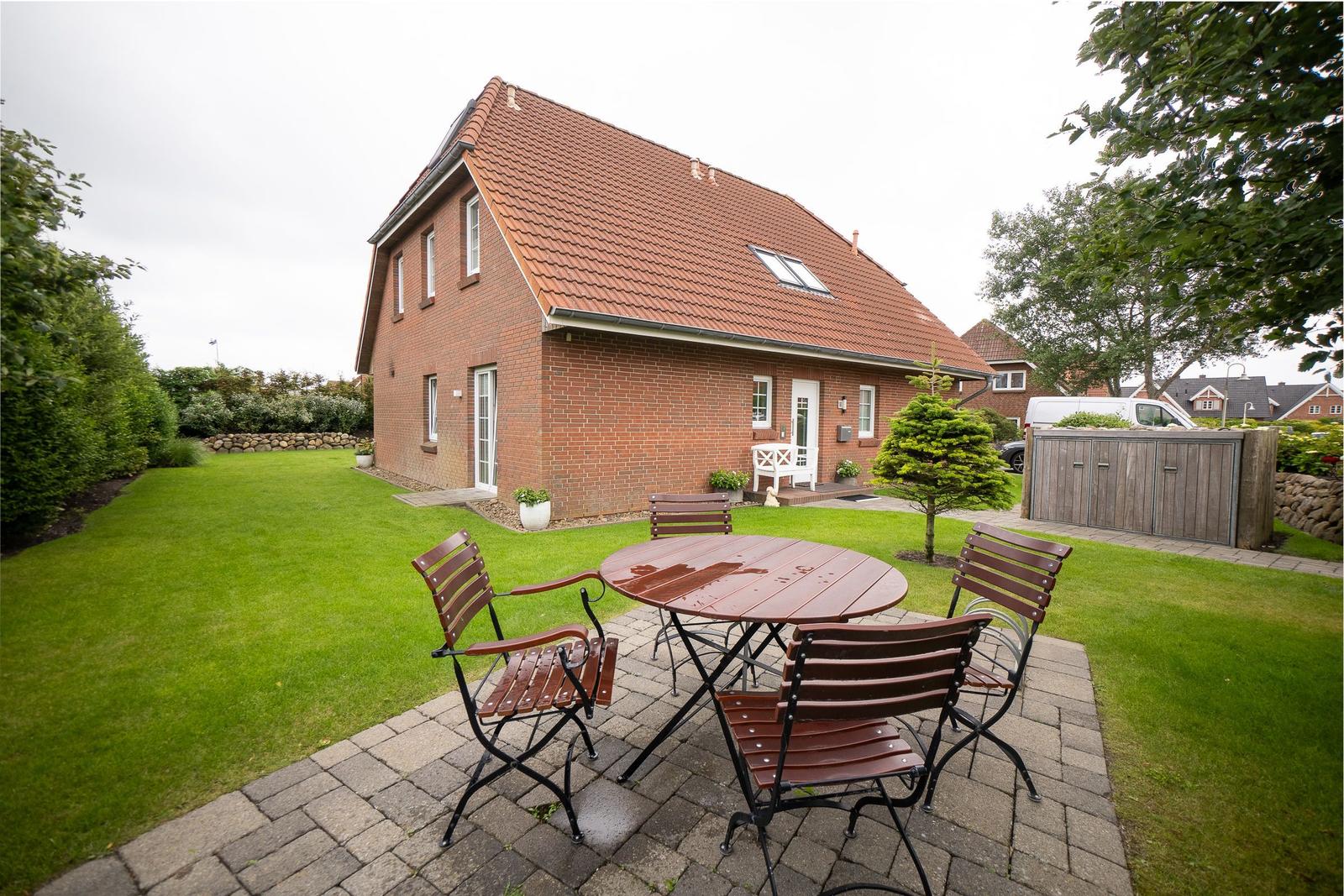 Rotes Ziegelhaus mit Garten und Terrasse mit Tisch und Stühlen.