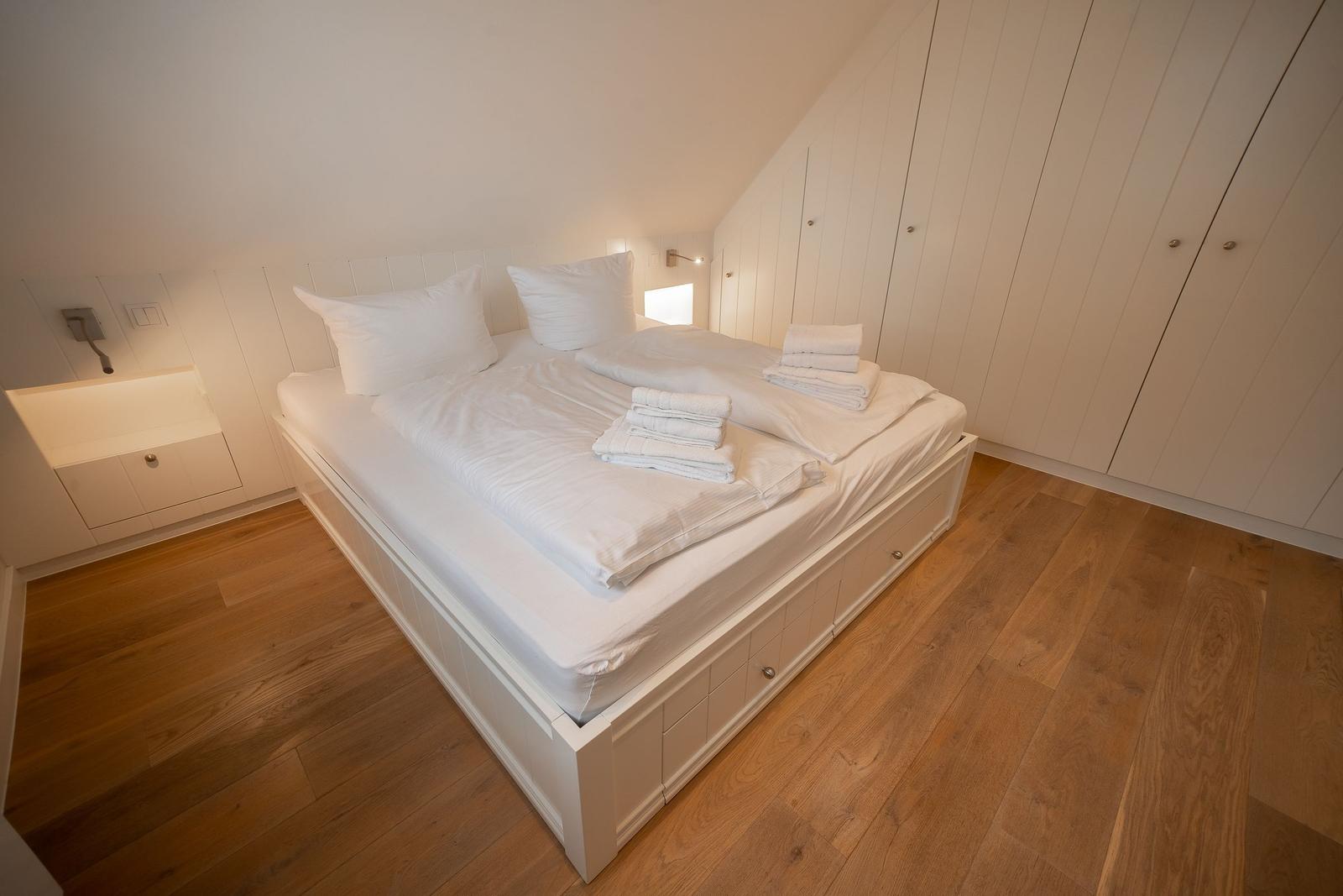 Schlafzimmer mit weißem Bett, Holzboden und Kleiderschrank.