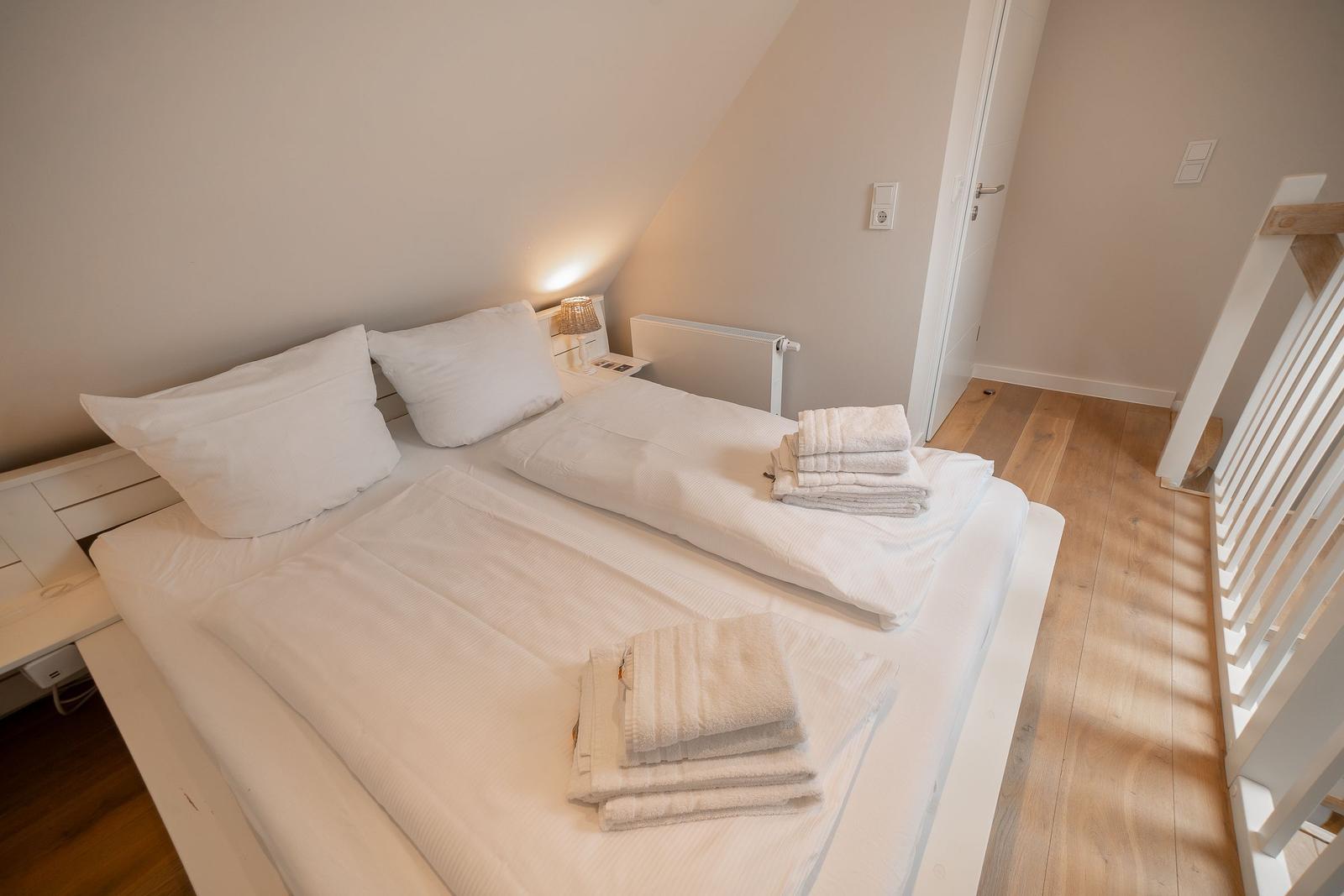Schlafzimmer mit weißem Bett, gefalteten Handtüchern und Holzboden.