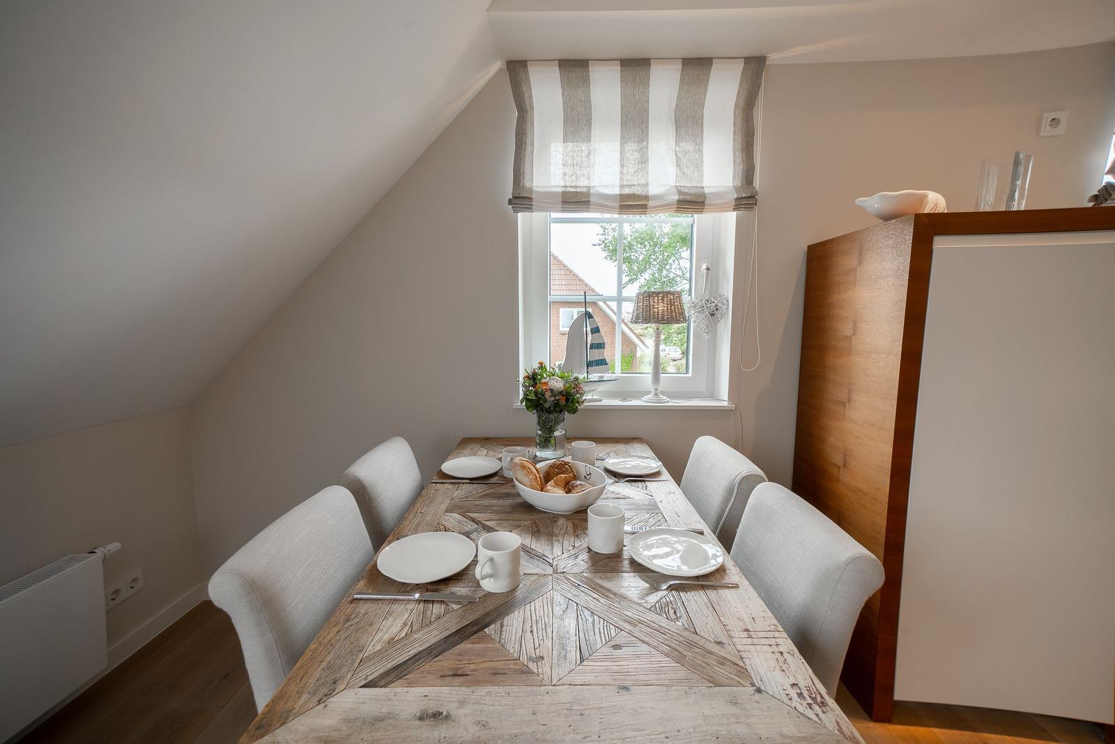 Esszimmer mit Holztisch, Stühlen und Fenster mit Blick nach draußen.