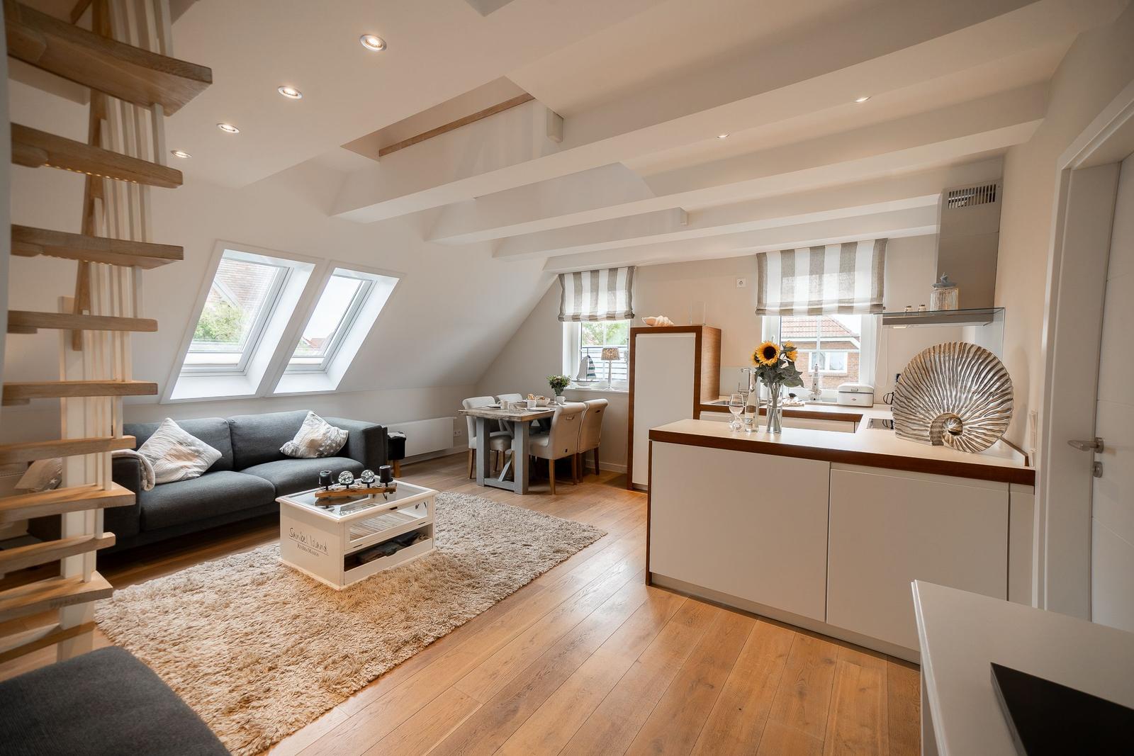 Wohn- und Essbereich mit Küche unter Dachschrägen. Holzfußboden, Sofa, Tisch und Küchenzeile.