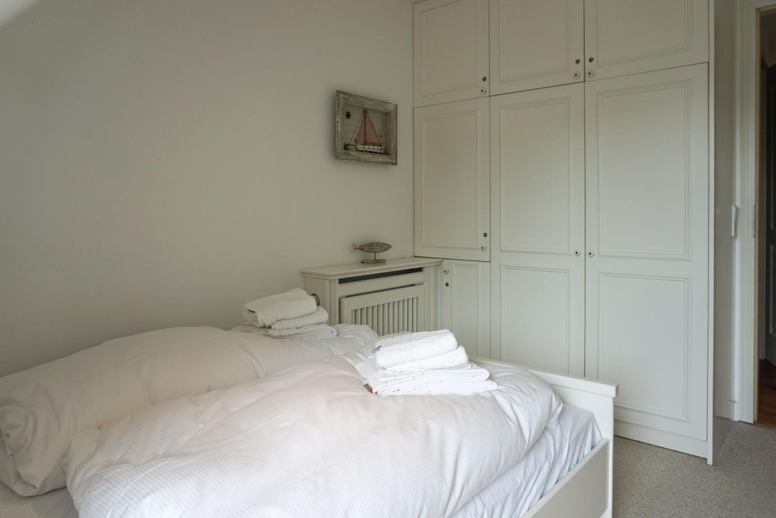 Bedroom with white bed, wardrobe, and wall picture with sailboat.