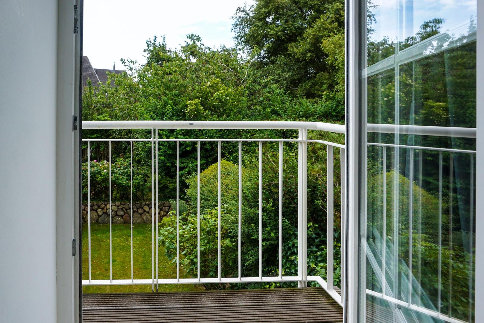 Balcony with white metal railing and view of green garden