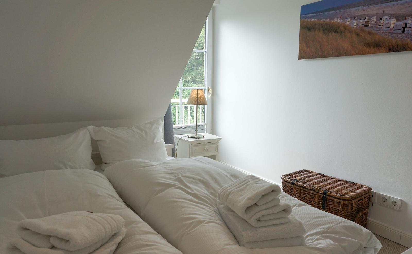 Bedroom with bed, nightstand, and basket. Window with view of green.