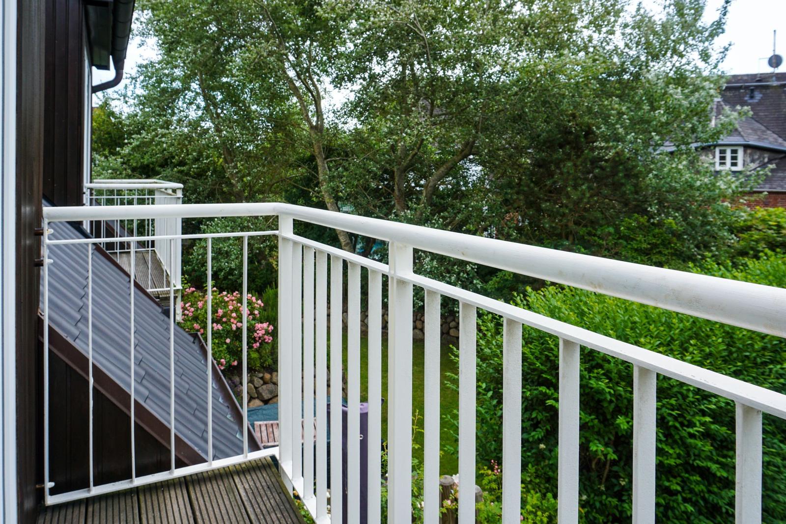 Terrace with white railing and view of green garden with flowers.