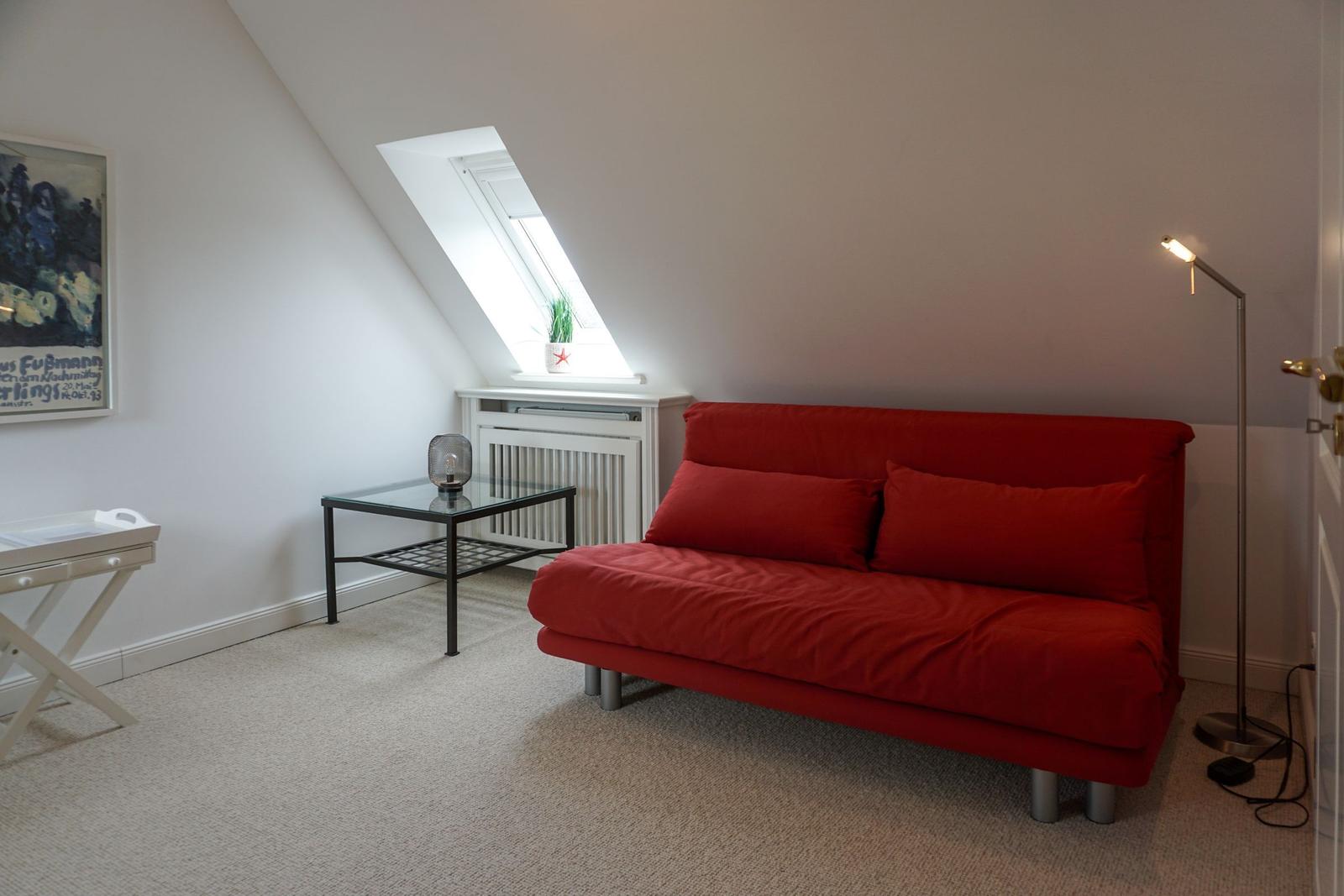 A room with red sofa, skylight, and floor lamp.