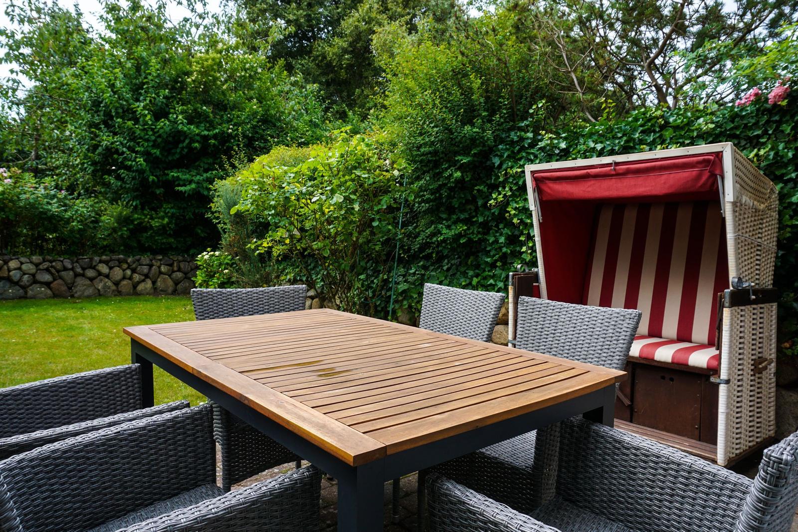 Terrace with table, chairs, and beach chair. Background: green garden with stone wall.