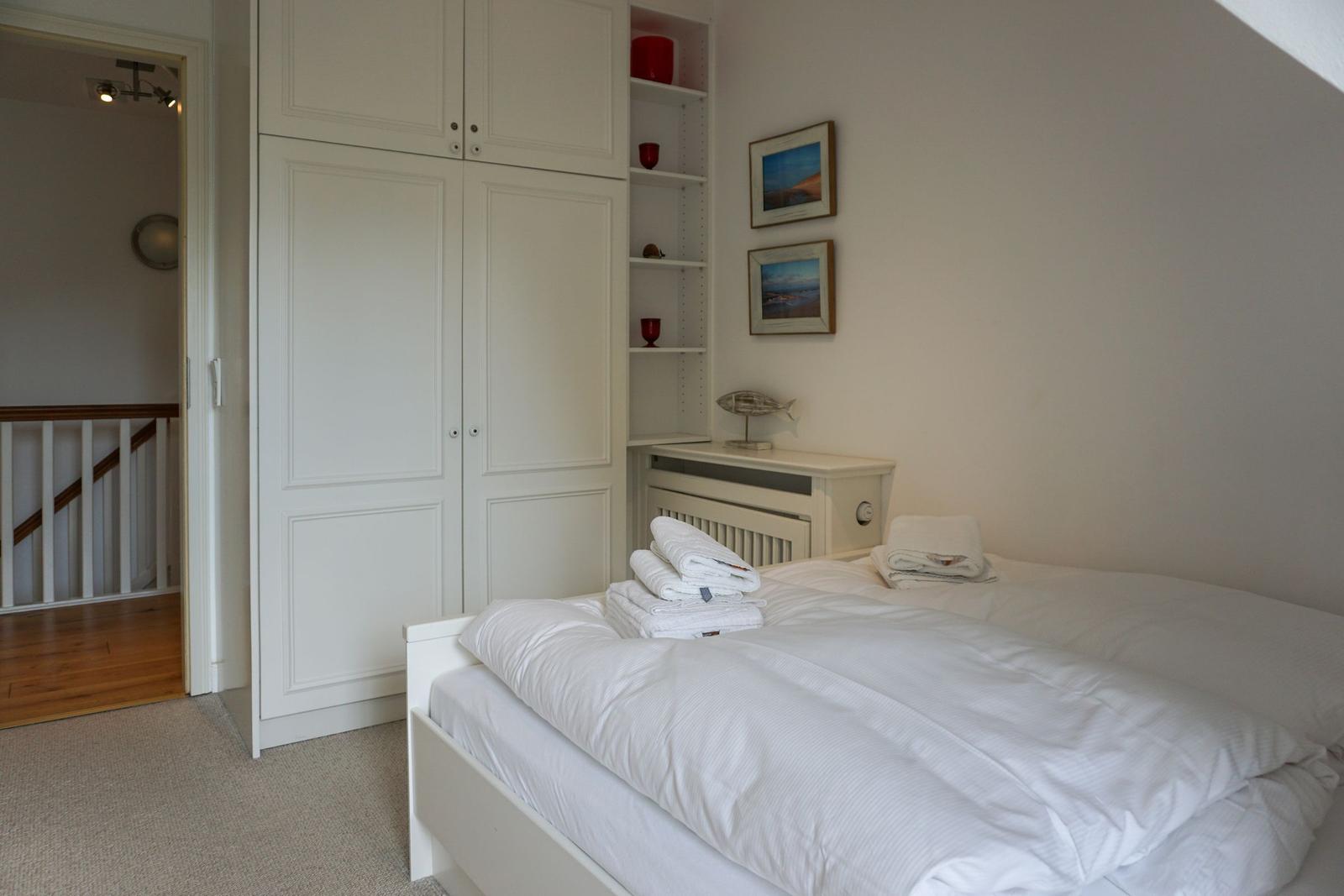 Bedroom with white bed, wardrobe, and wall pictures
