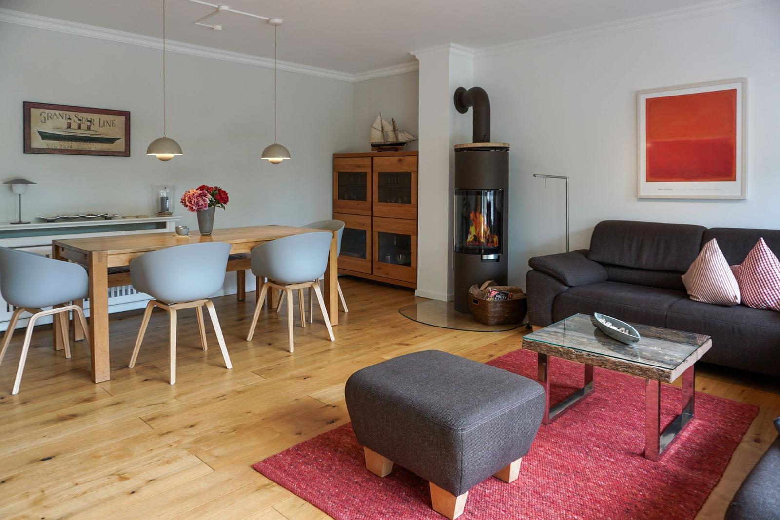 Living and dining area with wooden floor, sofa, dining table, and wood stove.