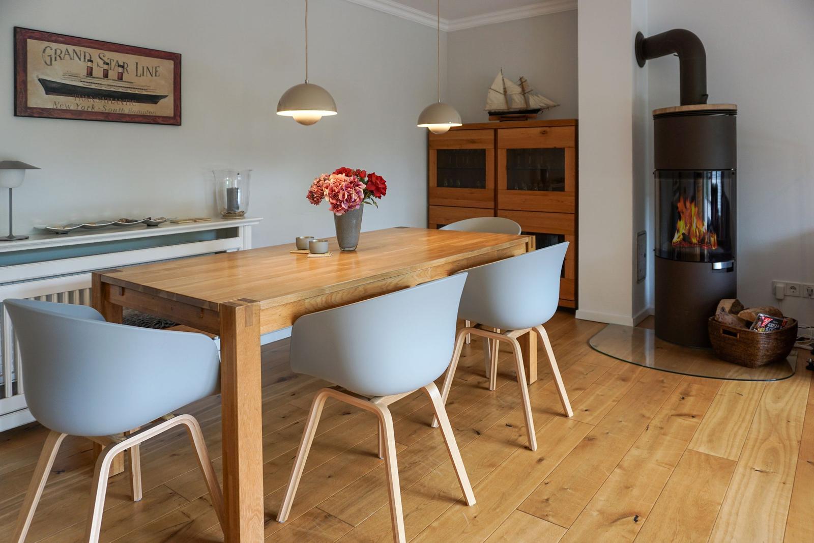 Dining room with wooden table, chairs, and wood stove. Wall art and ship model visible.