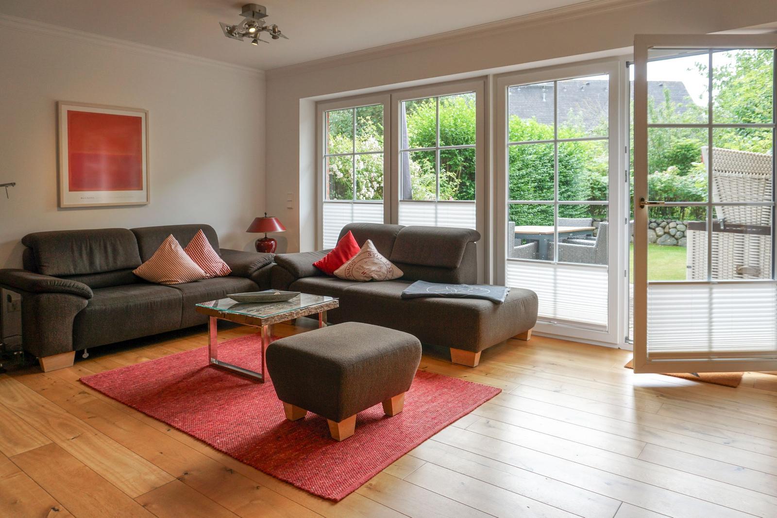 Living room with sofa, ottoman, and red rug. Entrance to terrace with garden.