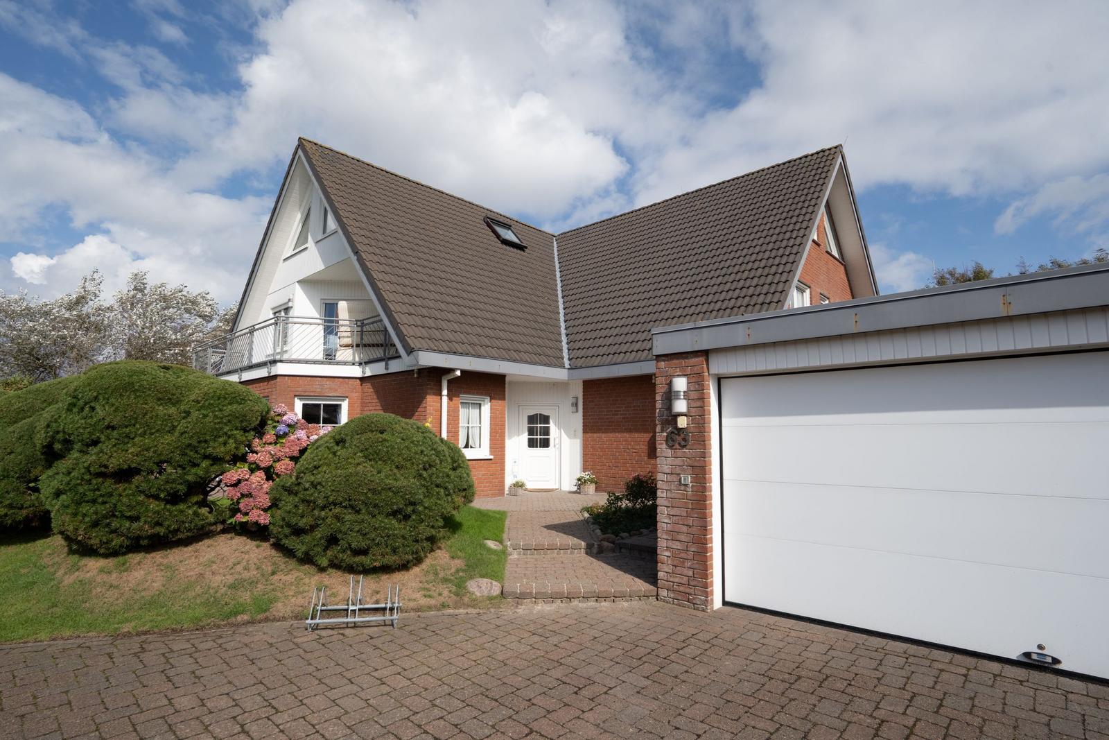 House with garage, balcony, and paved forecourt under blue sky.