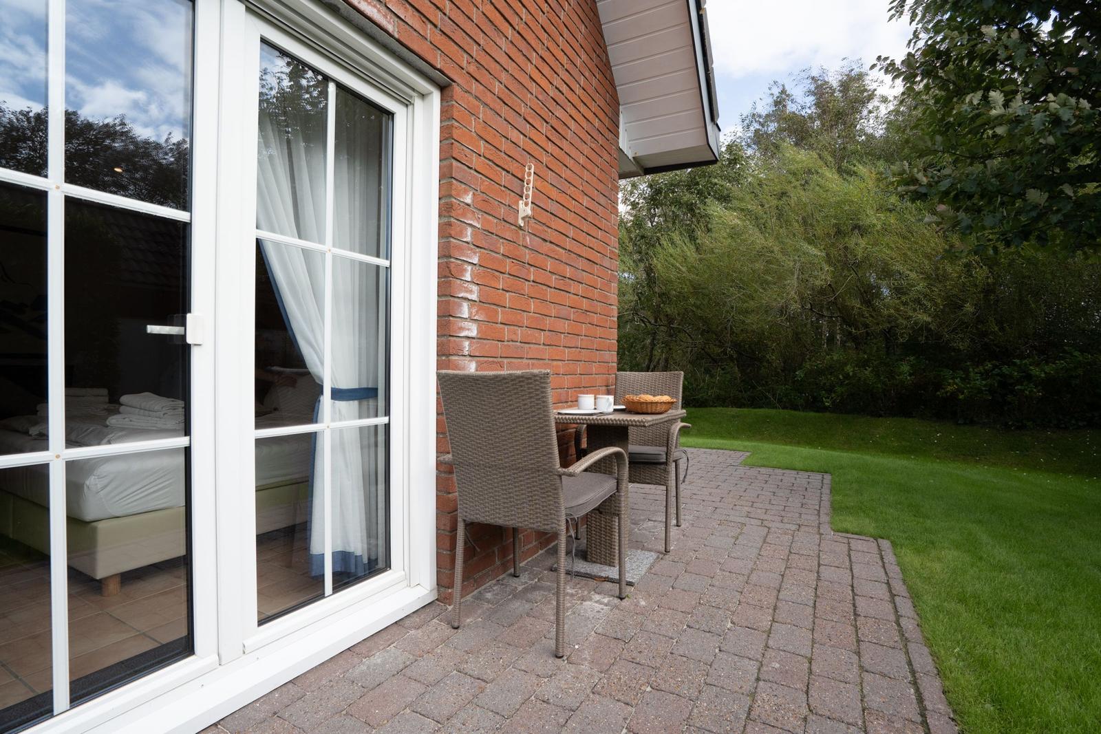 Terrace with table and chairs next to a bedroom with view of greenery.