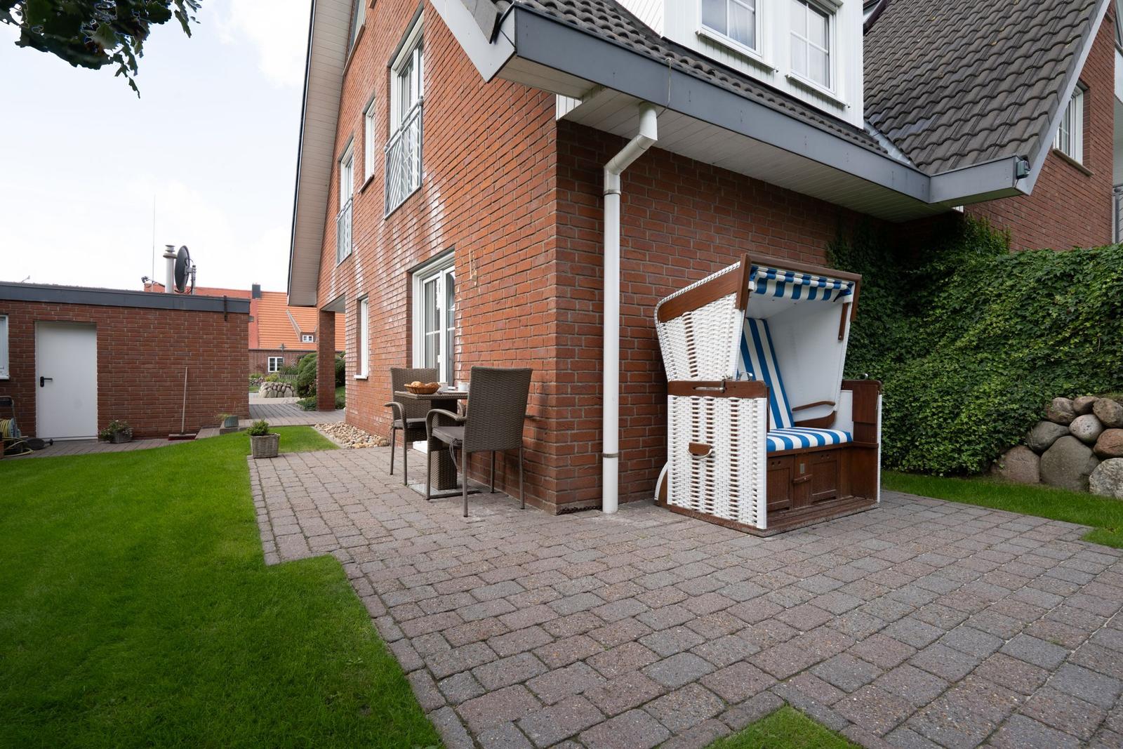 Terrace with beach chair, table and chairs in front of brick house.