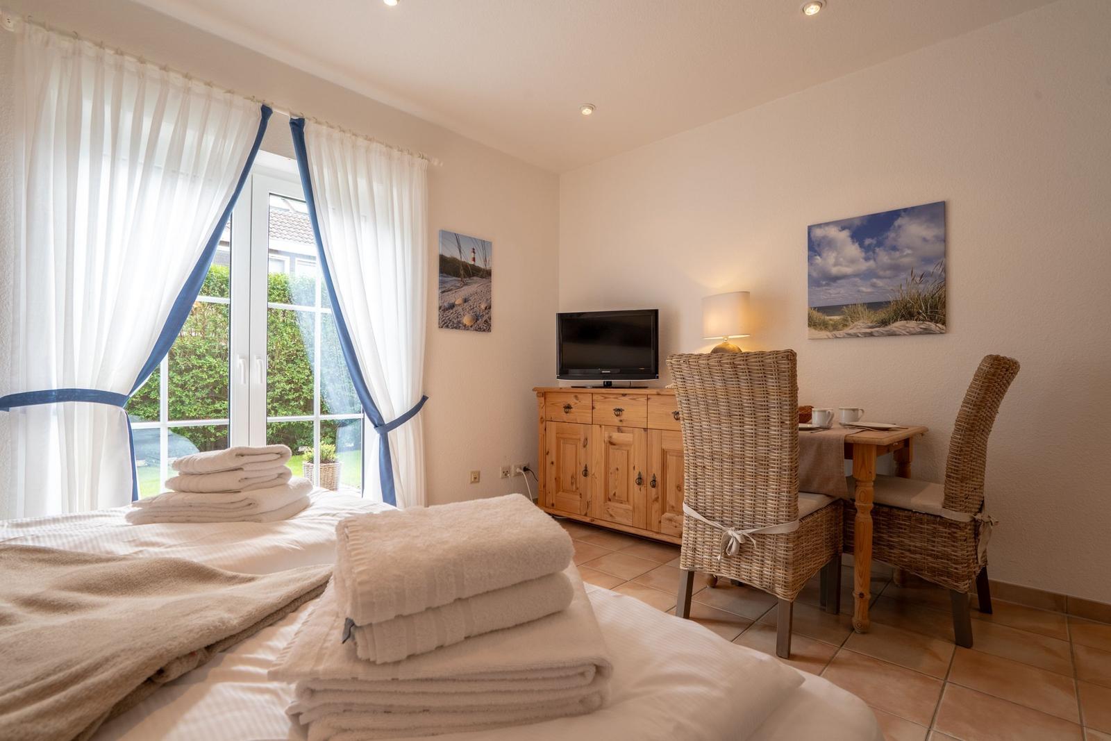 Bedroom with bed, TV, dining table, and garden view.