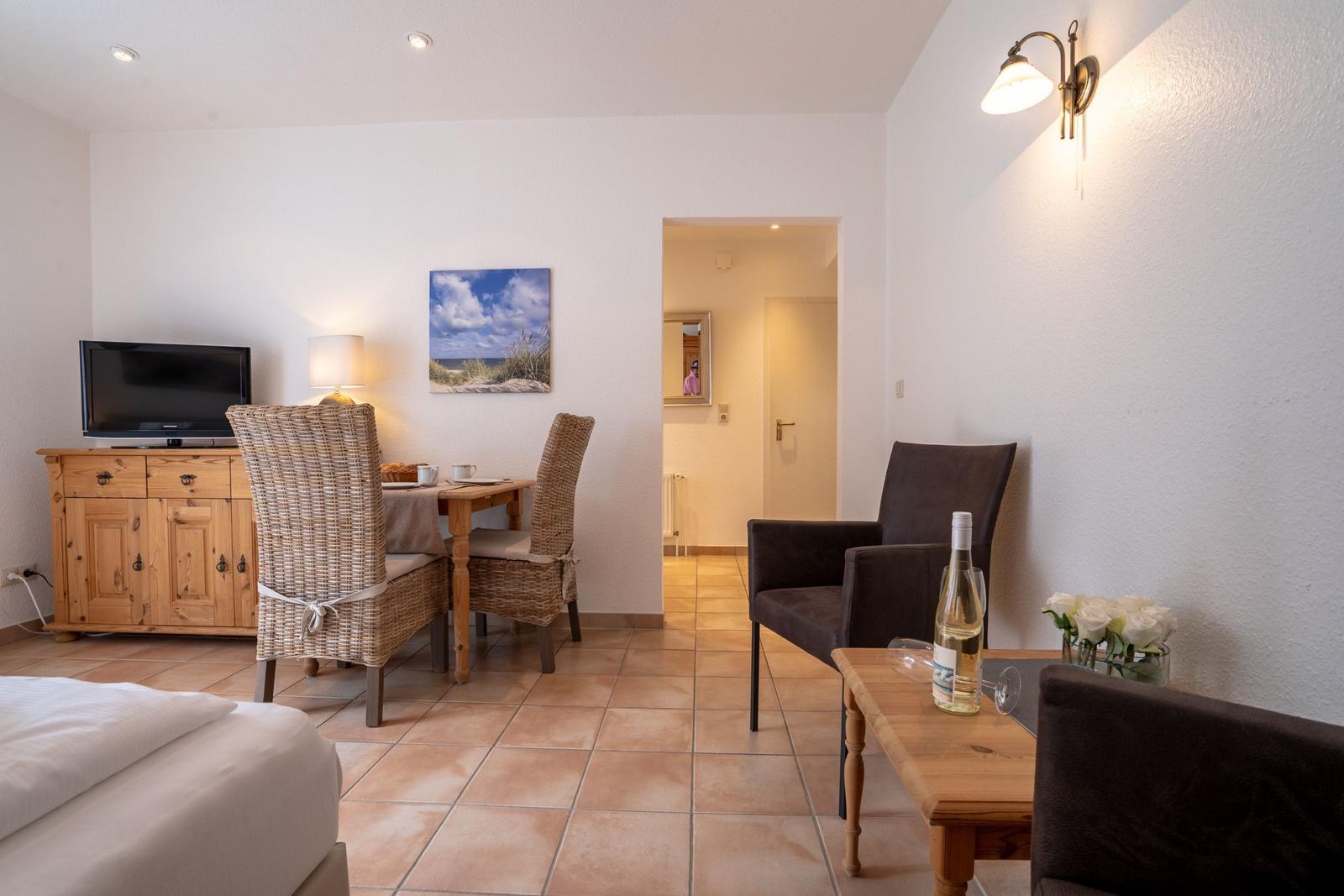 A room with sofa, table, chairs, and TV. Wall picture and tiled floor.