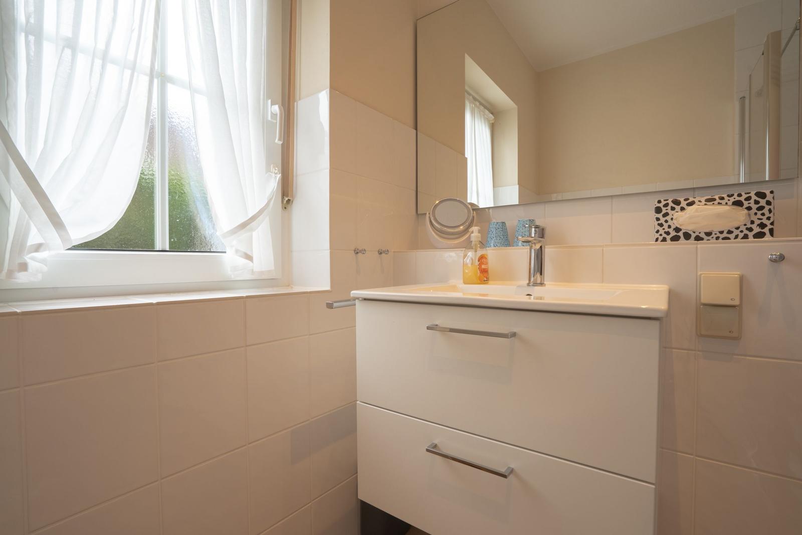 Bathroom with sink, mirror, and window with white curtains.
