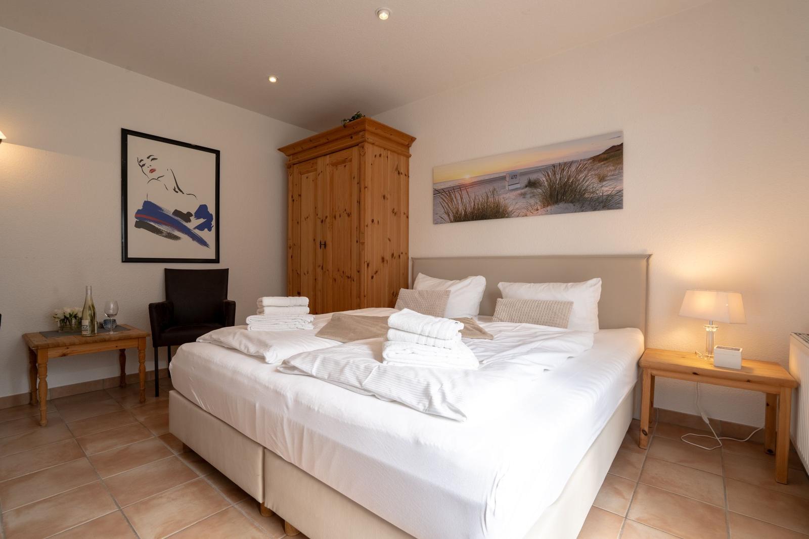 Bedroom with double bed, wooden wardrobe, and wall art.