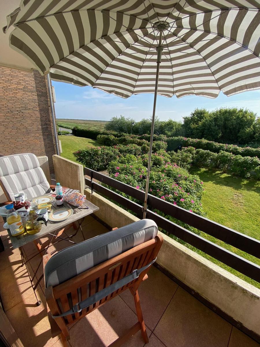 Terrace with umbrella, table and chairs. View of green garden and flowers.