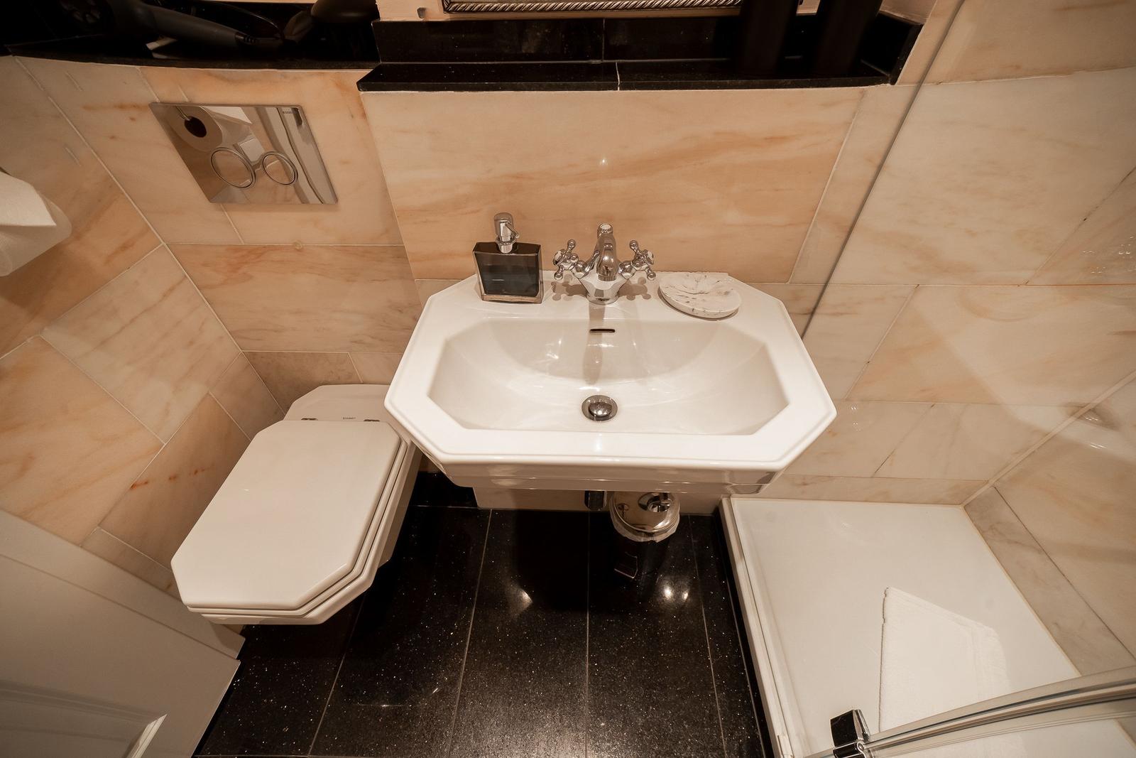 Bathroom with sink, toilet, and shower. Marble tiles and black floor.