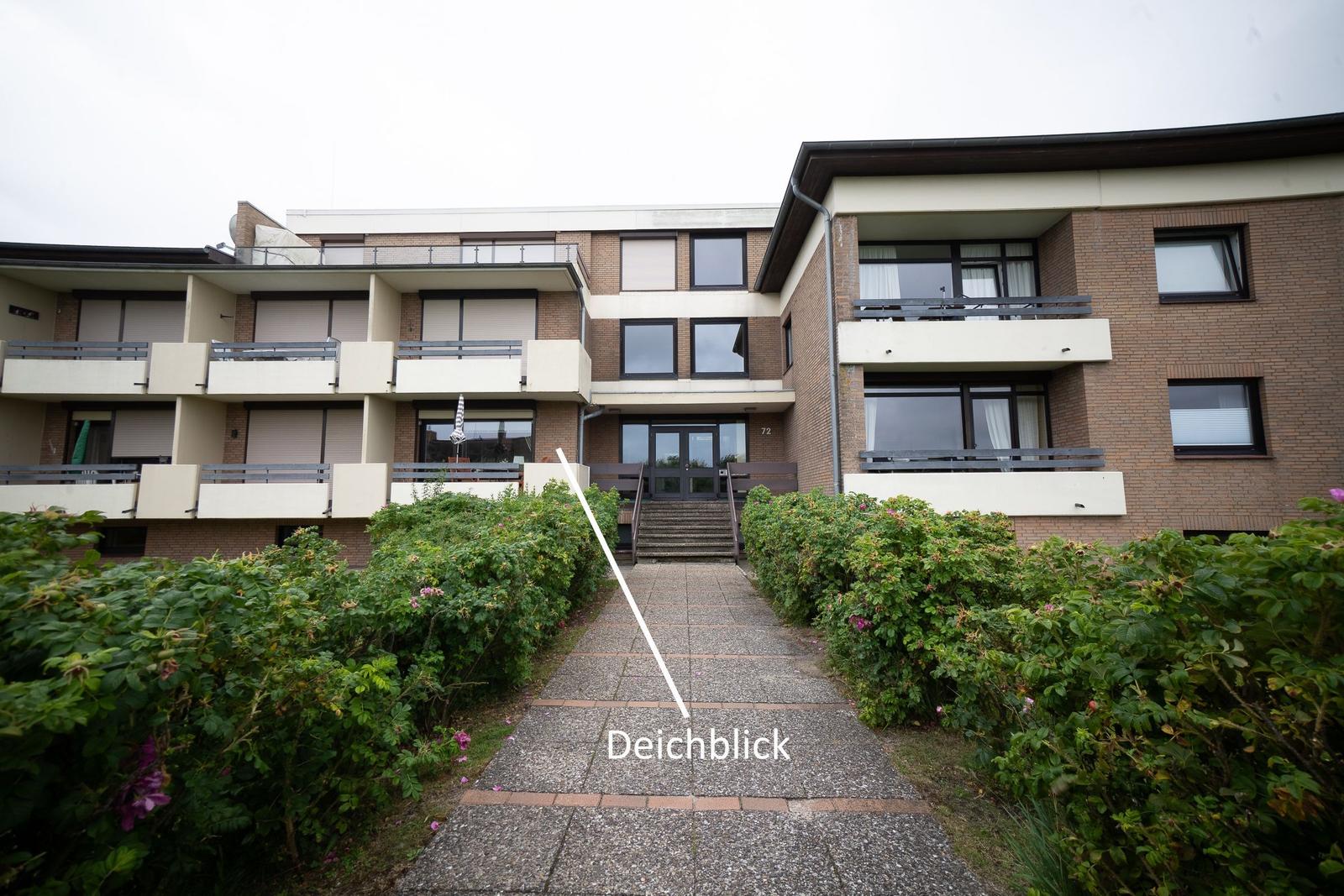 House with balconies and paved pathway through green hedges.