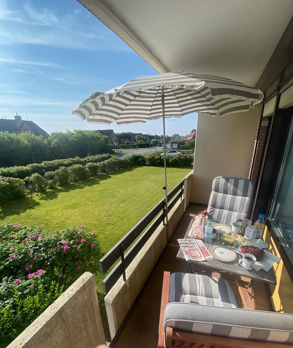 Terrace with umbrella, table and chairs. View of green lawn and flowers.