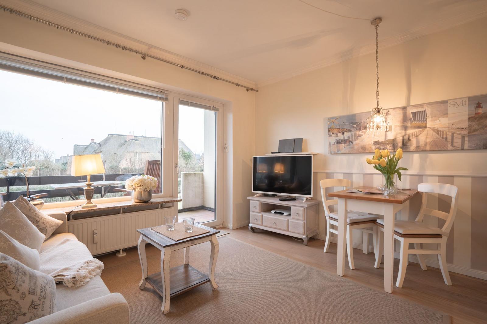 Living and dining area with TV, table, chairs, and view of balcony.