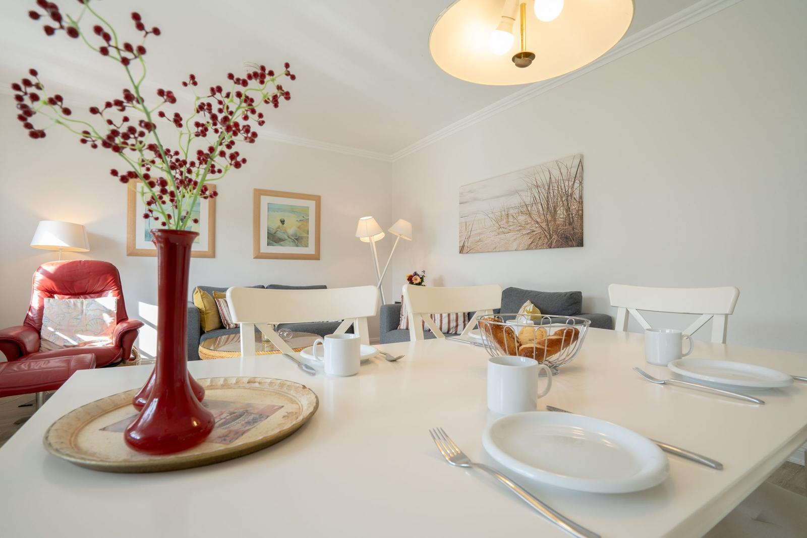 Esstisch mit Stühlen, roter Vase und Wandbildern im Wohnbereich.