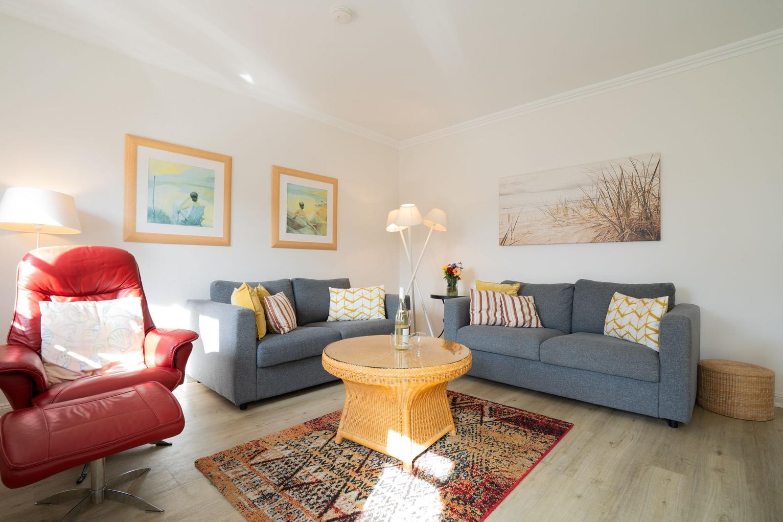 Wohnzimmer mit grauem Sofa, rotem Sessel und runden Couchtisch.