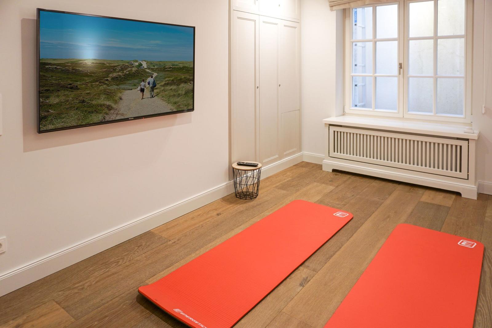 Two red yoga mats on wooden floor, wall-mounted TV, and window with radiator.