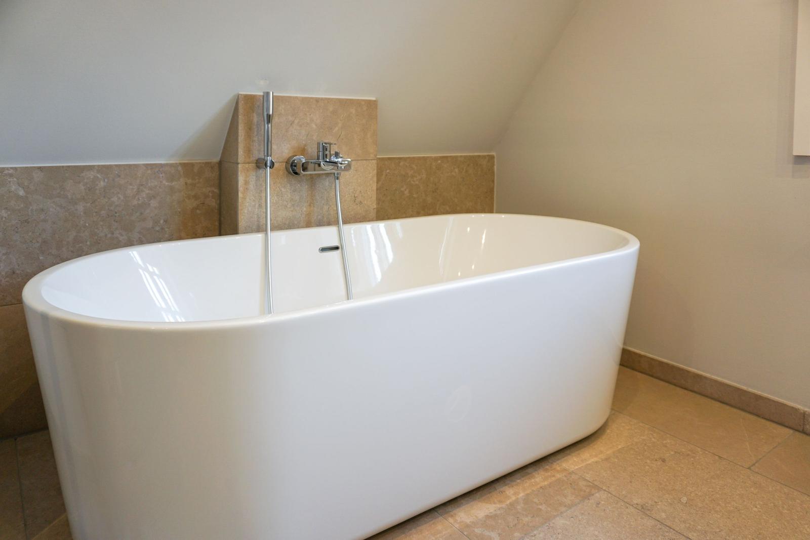 Freestanding bathtub with showerhead in bathroom with stone wall